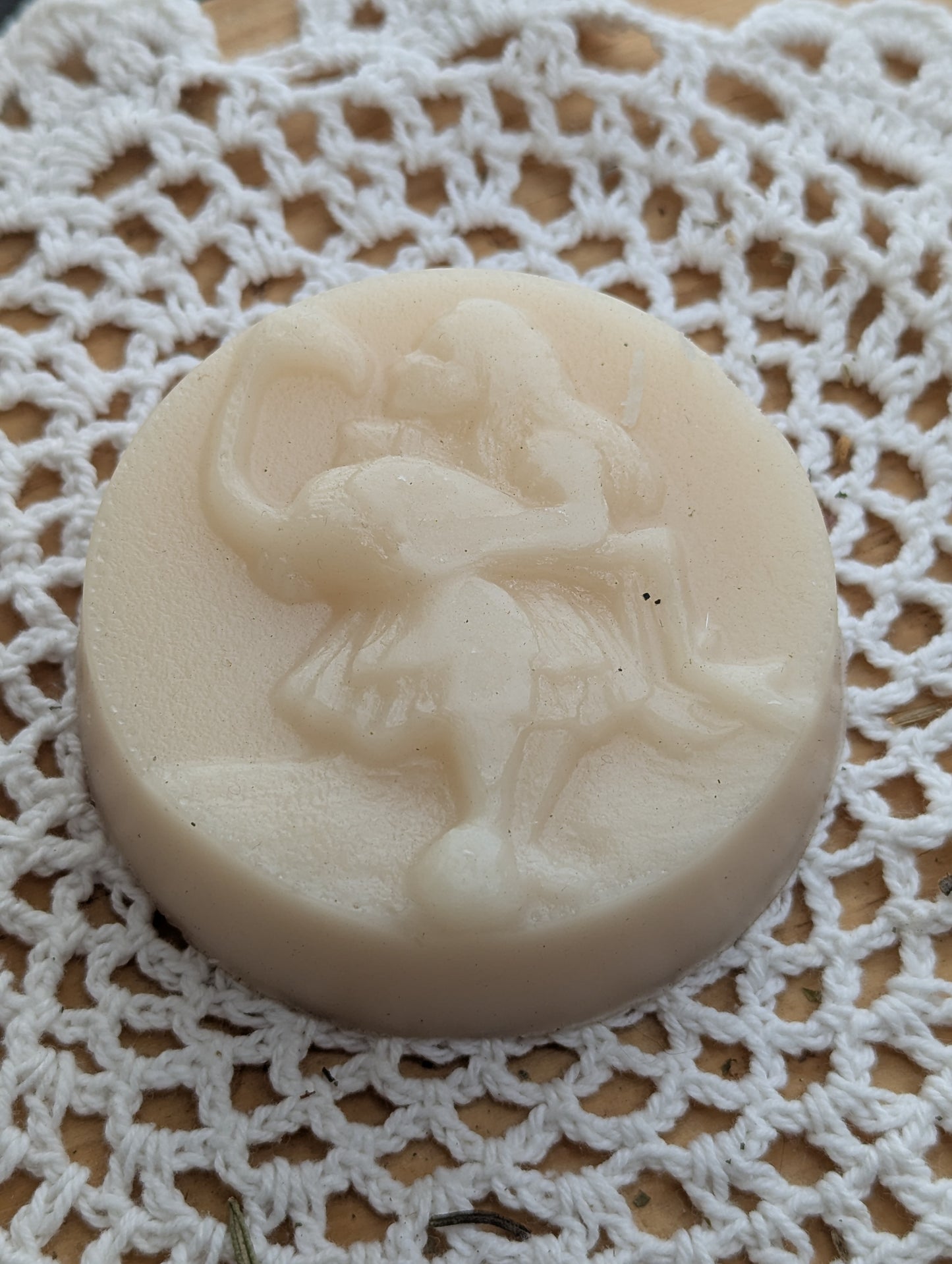 Hair conditioner soap bar with a design of a girl akin to Alice from Alice in Wonderland kissing a flamingo she is holding, on a white lace background.