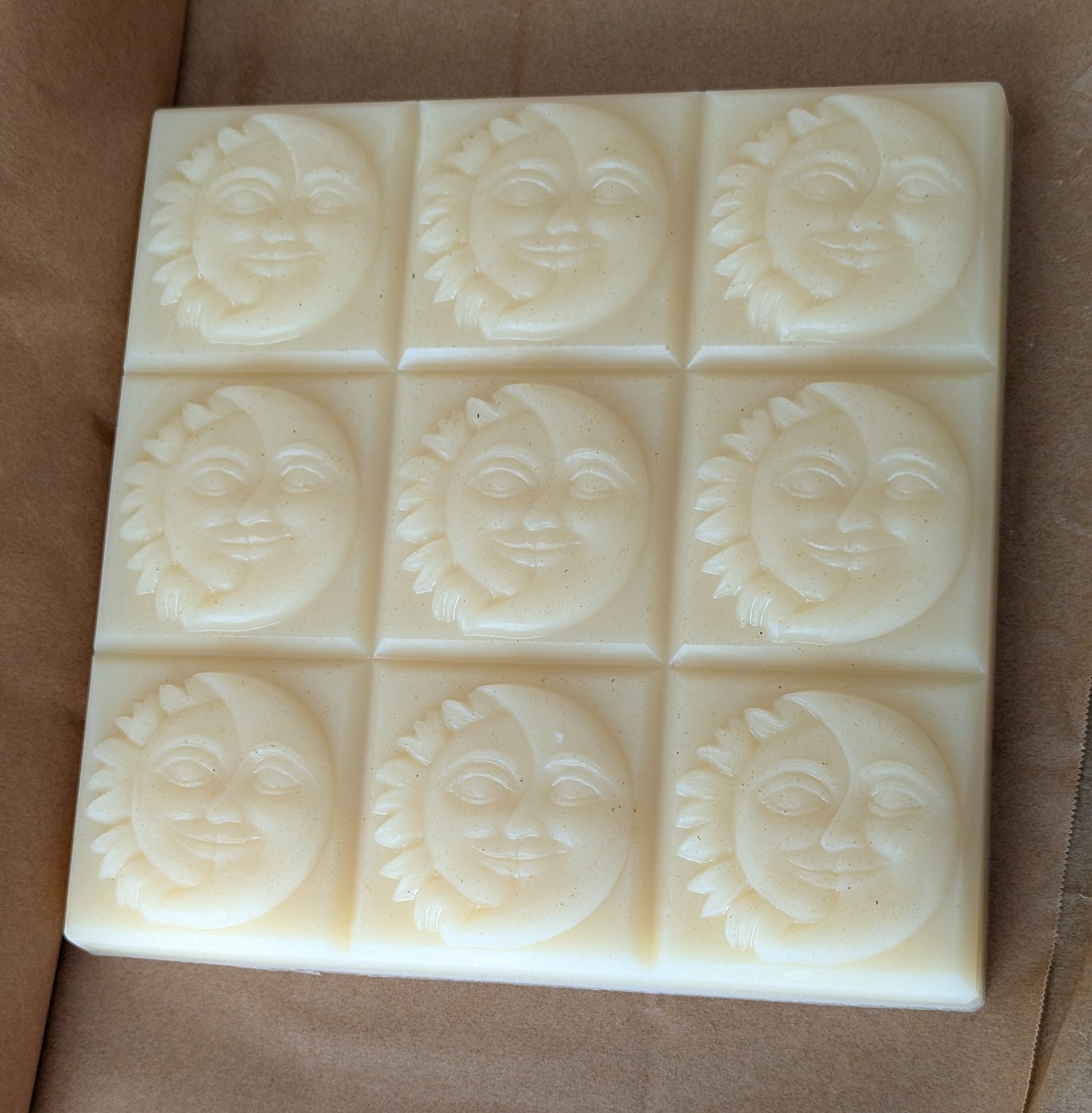 Block of 9 facial soap bars with sun and moon face designs on a brown parchment paper background