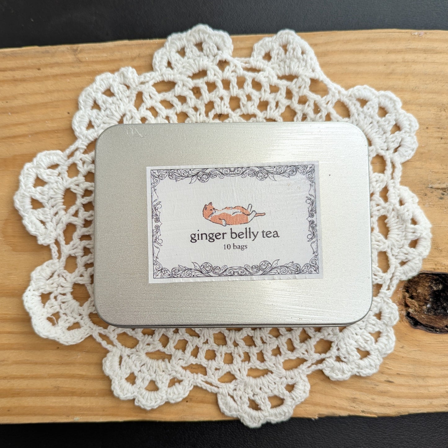 Small tin labeled 'ginger belly tea' on a white doily with a black background