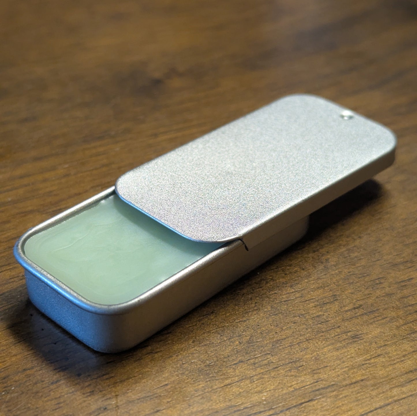 Small metal tin with a green herbal mint lip balm inside on a wooden surface