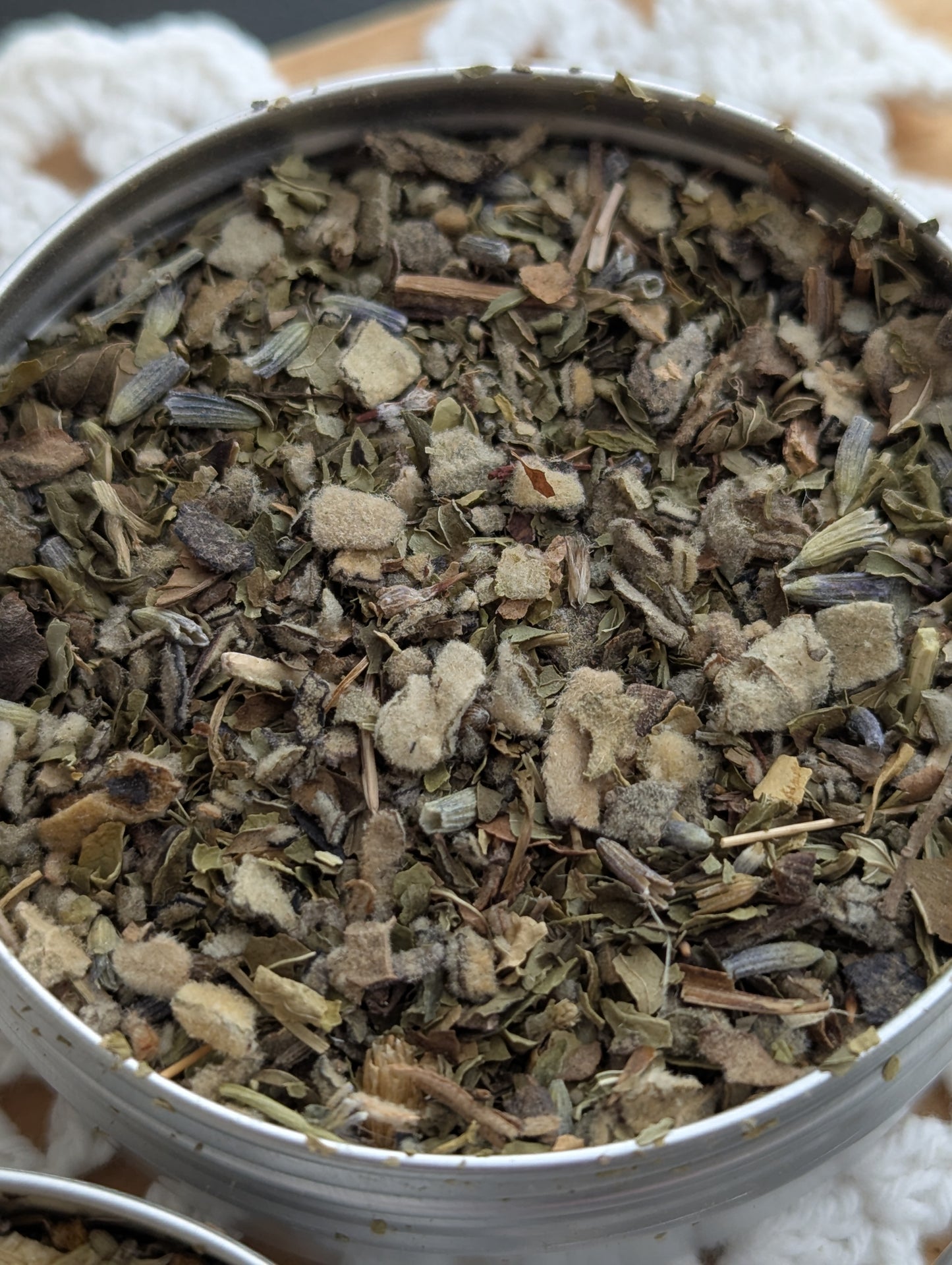 Close-up of a metal tin filled with dried herbs on a white textured background