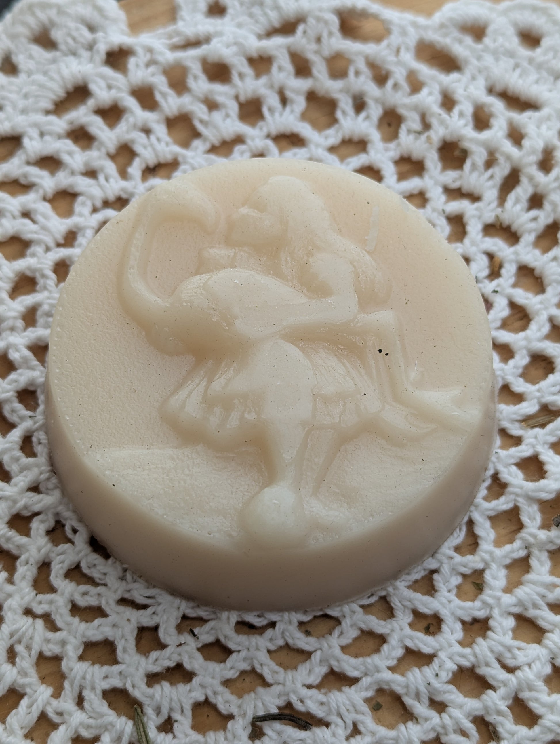 Hair conditioner soap bar with a design of a girl akin to Alice from Alice in Wonderland kissing a flamingo she is holding, on a white lace background.