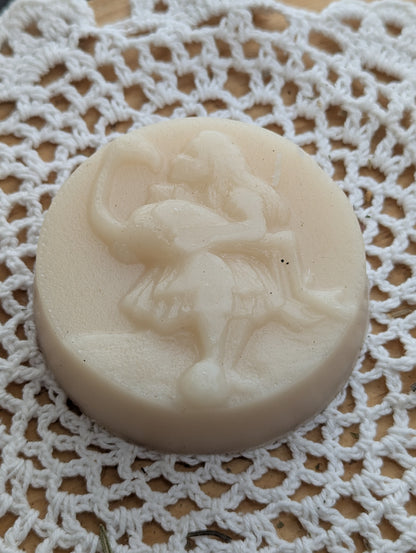 Hair conditioner soap bar with a design of a girl akin to Alice from Alice in Wonderland kissing a flamingo she is holding, on a white lace background.