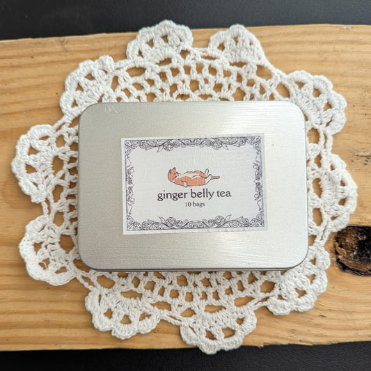 Small tin labeled 'ginger belly tea' on a white doily with a black background
