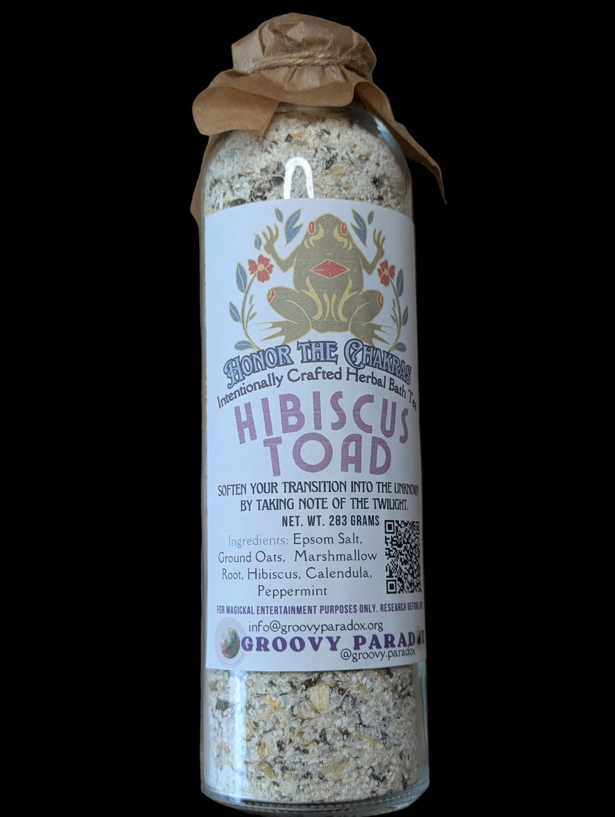 A glass jar of Groovy Paradox 'Hibiscus Toad' herbal tea blend, sealed with a brown parchment paper band and wrapped in a white label featuring a mystical toad flower illustration, set against a brown background.
