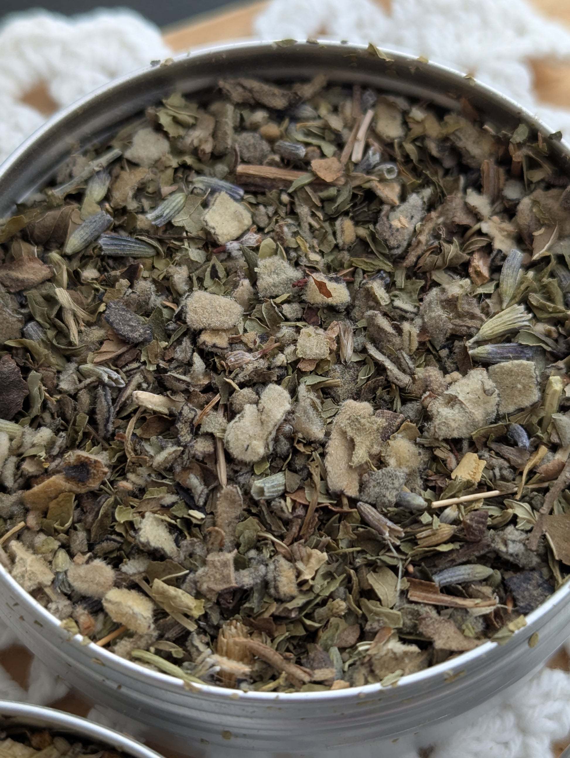 Close-up of a metal tin filled with dried herbs on a white textured background