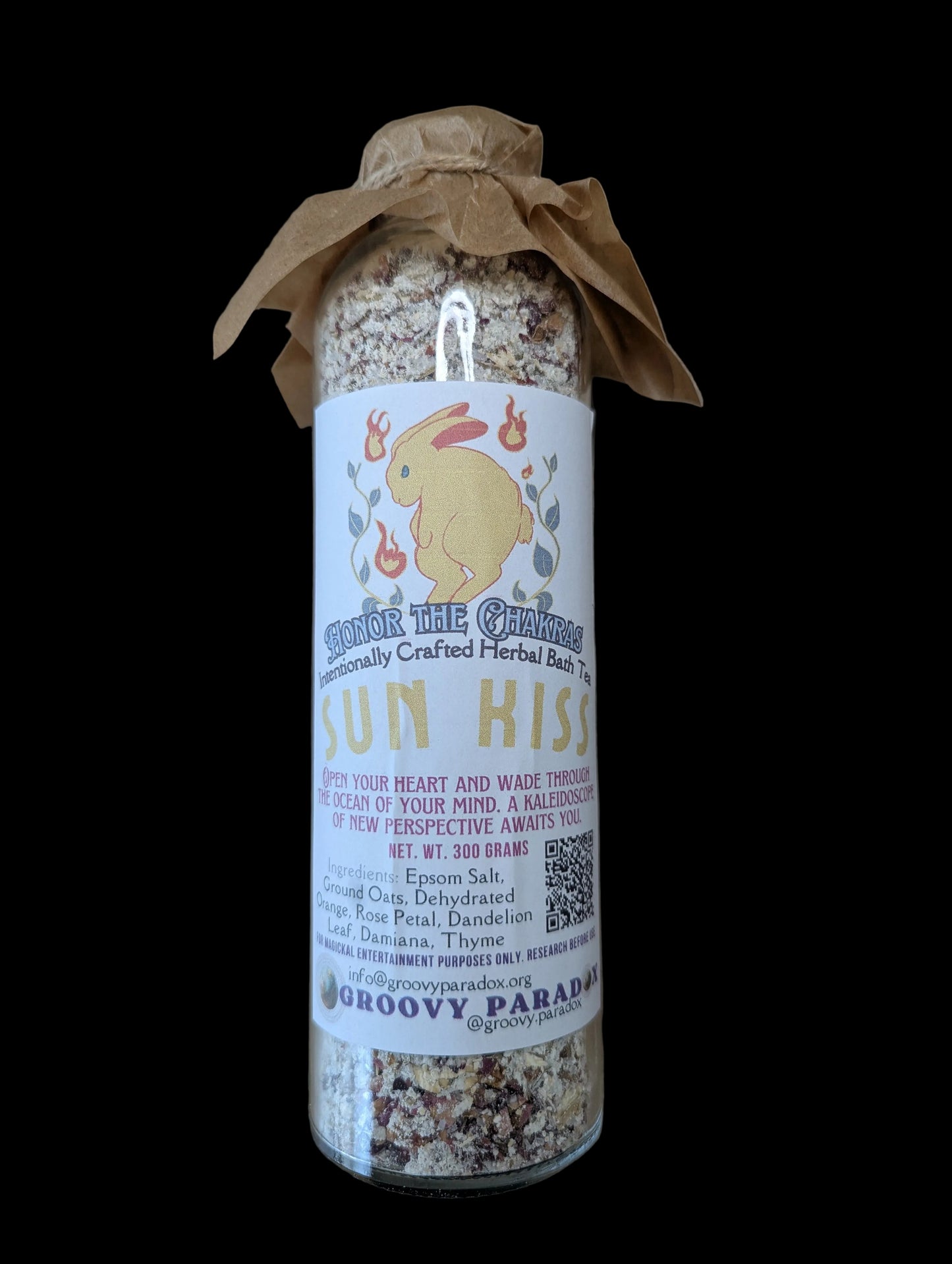 A glass jar filled with dried herbs or spices, wrapped in a brown paper band and a white label featuring a yellow bunny and the text 'Sun Kiss' and 'Groovy Paradox', placed on a brown background.