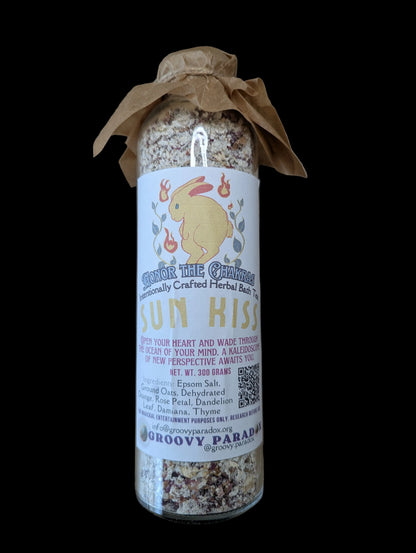 A glass jar filled with dried herbs or spices, wrapped in a brown paper band and a white label featuring a yellow bunny and the text 'Sun Kiss' and 'Groovy Paradox', placed on a brown background.